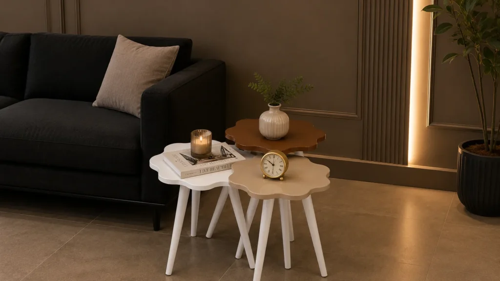 Three-piece flower-shaped nesting sculptural side tables for living room in pastel tones alongside a dark charcoal couch.